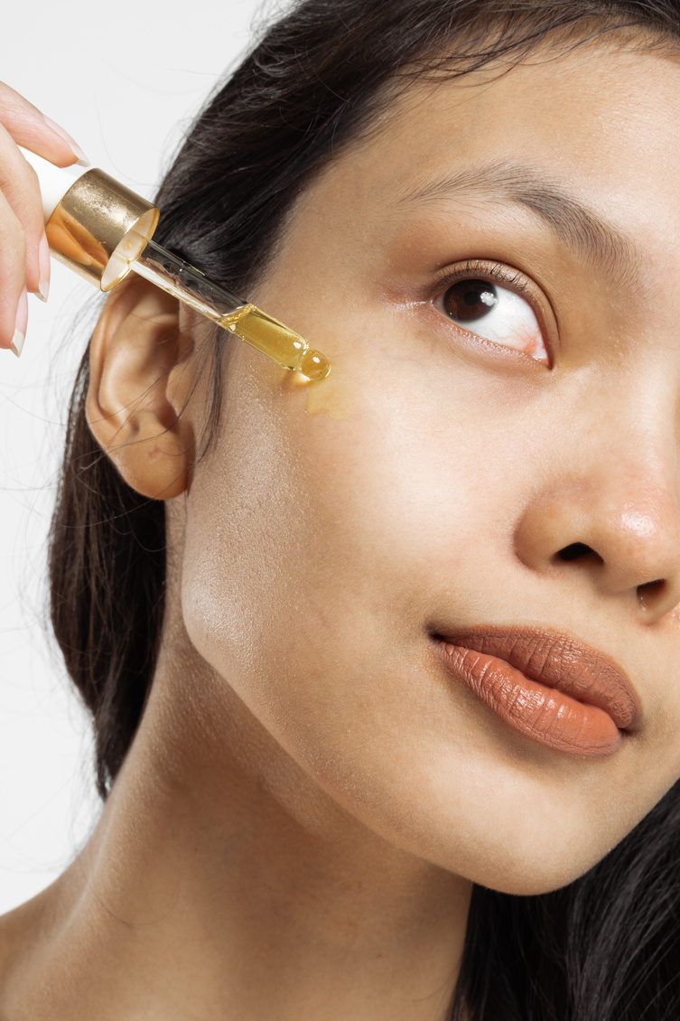 Closeup Portrait of Woman Applying Oil on Face with Dropper